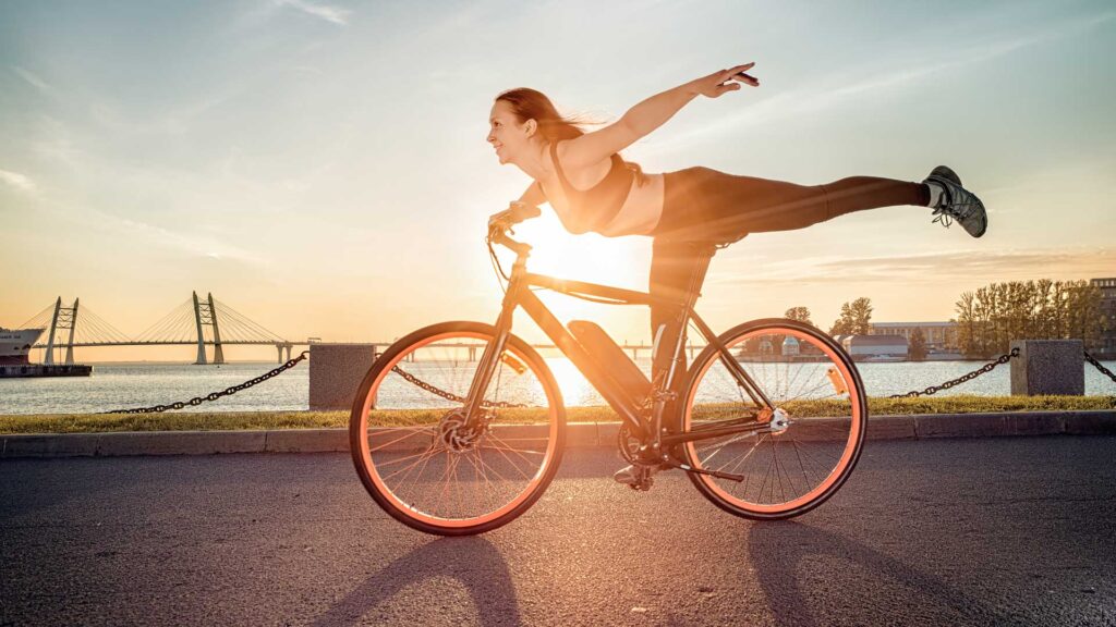 Frau in Fitnesskleidung fährt glücklich Fahrrad, ein Bein ausgestreckt und die Arme offen – Fahrradfahren ist gesund und macht frei. Frau in Fitnesskleidung fährt glücklich Fahrrad, ein Bein ausgestreckt und die Arme offen – Fahrradfahren ist gesund und macht frei.