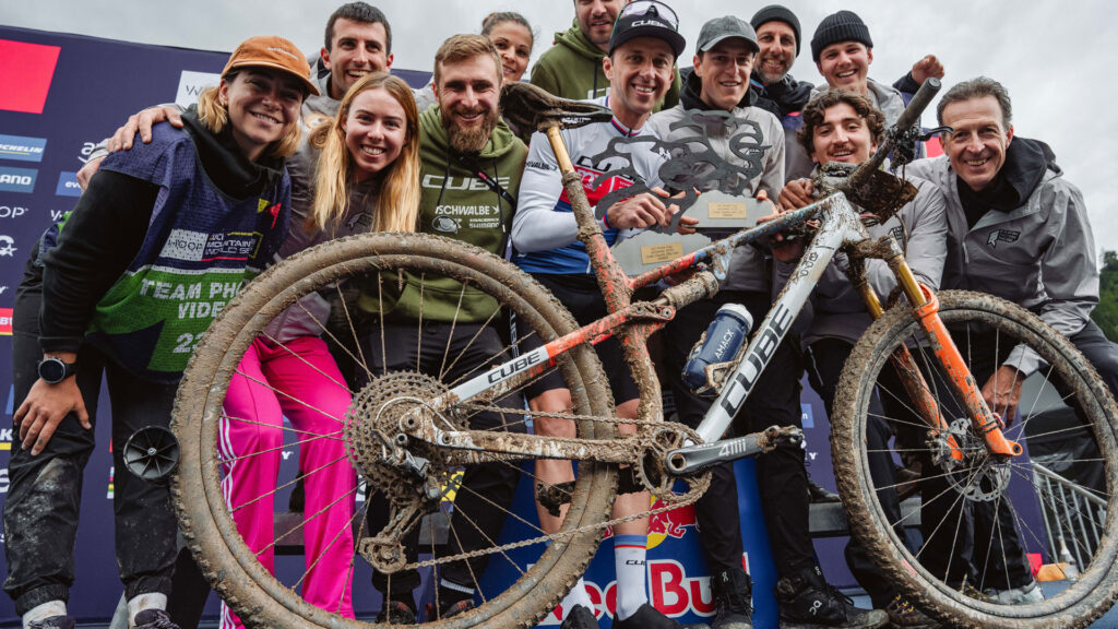 Finn Treudler mit dreckigem CUBE Fully vor dem Podium nach seinem U23-XCO-Sieg in Leogang 2025, gemeinsam mit dem CUBE Factory Racing Team