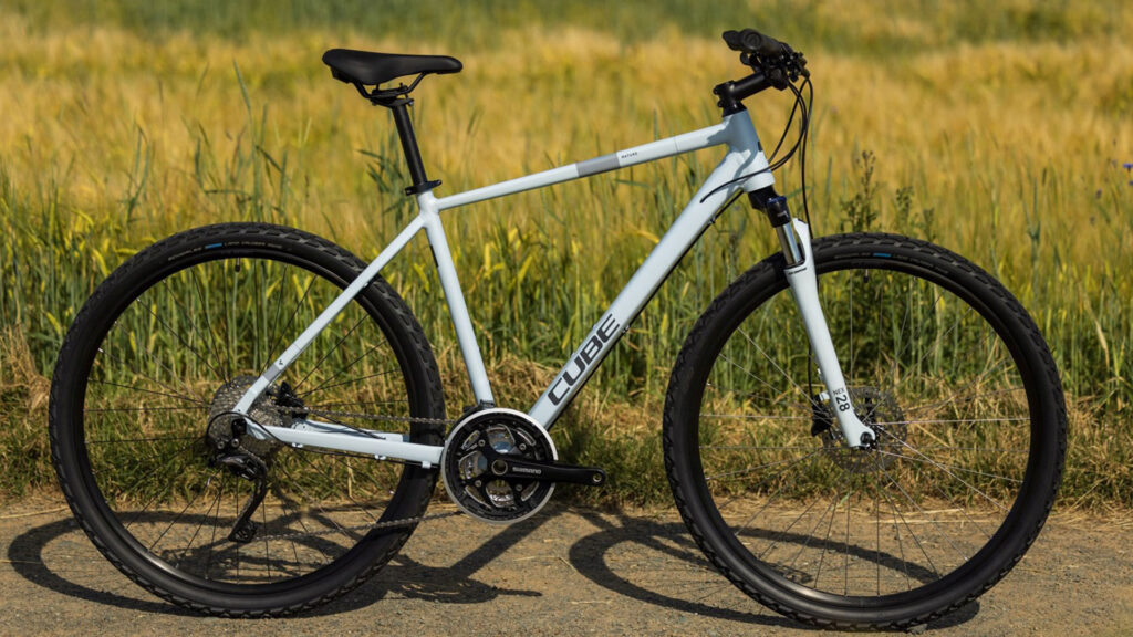 Cube Nature Crossbike auf Feldweg &ndash; sportliches Fahrrad vor gr&uuml;n-gelbem Wiesenhintergrund