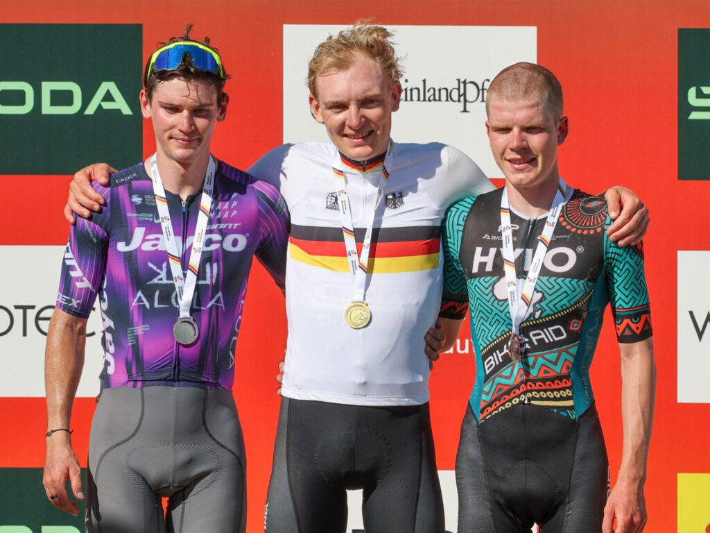 Georg Zimmermann mit Goldmedaille umarmt den Zweit- und Drittplatzierten nach dem Sieg bei der Deutschen Stra&szlig;enradmeisterschaft 2025