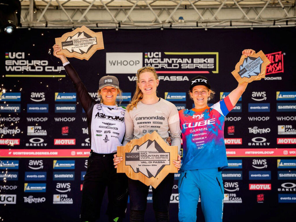 Simona Kuchynkova auf dem Podium des Enduro World Cups in Canazei, hebt mit dem linken Arm ihre Troph&auml;e hoch, neben der Zweit- und Drittplatzierten