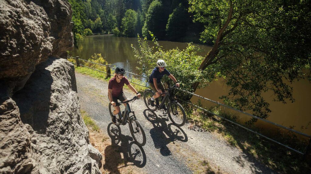 Mann und Frau fahren gemeinsam auf einem Cube 2026 Reaction Hybrid E-Mountainbike durch die Natur.