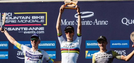 Finn Treudler jubelt beim Cube Factory Racing Saisonfinale 2025 in Mont-Sainte-Anne mit der Trophäe in den Händen, flankiert von dem Zweit- und Drittplatzierten auf dem Podium.