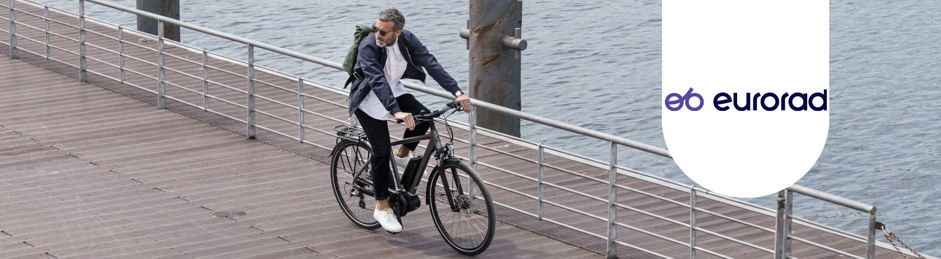 Ein Mann fährt mit seinem E-Bike auf einer Brücke. Neben ihm ist das eurorad-Logo zu sehen.