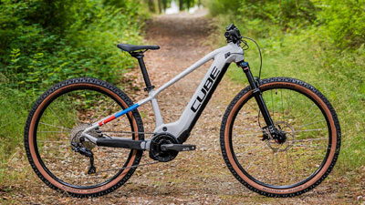 Zu sehen ist ein weißes Cube Kinder E-Bike, mit kleinem Detail in blau und rot. Es steht auf einem bewachsenem Waldweg.