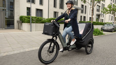 Eine Frau fährt mit einem grauen Lastenrad durch ein Wohngebiet.