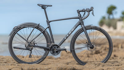 Zu sehen ist ein schwarzes Cube Gravel Bike, es steht auf felsiger Landschaft, im Hintergrund ist die Küste.