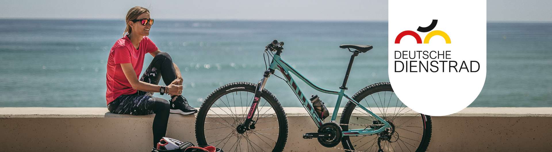 Eine Frau sitzt auf einer Mauer. Neben ihr steht ein blaues Mountainbike. Rechts daneben befindet sich das deutsche Dienstrad-Logo.